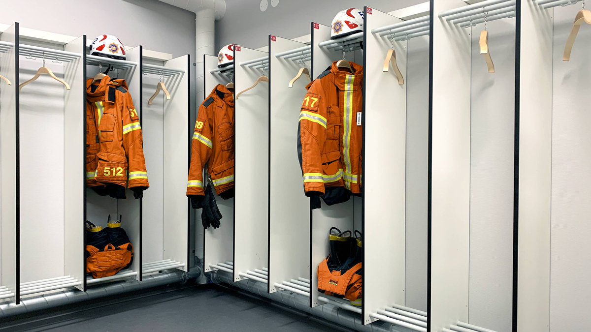Bilde som viser hjørnet i en garderobe, med innredning for utrykningspersonale. Innredningen er hvit og bildet viser oransje uniformer som er hengt opp i garderoben.