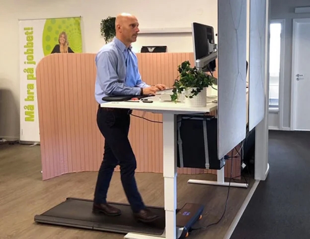 En mann i dress går på en gåmølle mens han jobber på datamaskinen ved pulten sin på kontoret.
