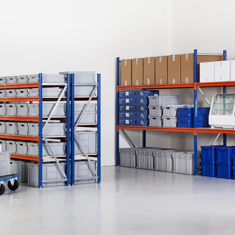 Orange og blå hyller med pappesker og stålkasser i forskjellige størrelser på en stort og rent lagerlokale med grått golv og hvite vegger.
