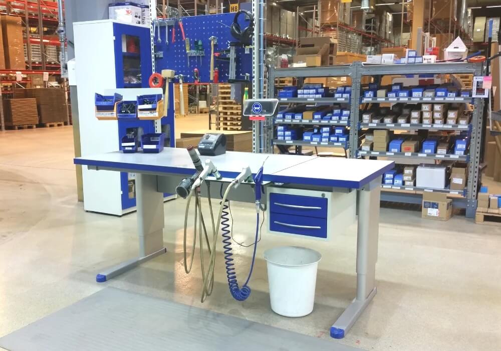 Et heve senke pakkebord i hvit og blå, som står midt i et lagerlokale, med strekkodelesere, verktøy-oppheng og alt tilbehør som trengs.